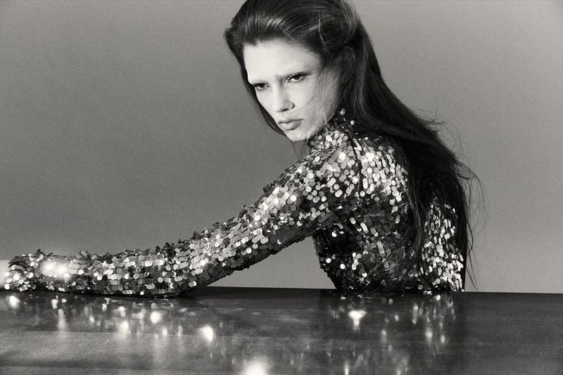 Model Wilda Rubin in a long-sleeve sequined top leaning on a reflective surface in a black and white editorial portrait.