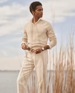 Model Stan Taylor wearing a beige knit sweater and cream trousers holding sunglasses outdoors for Ralph Lauren Purple Label.