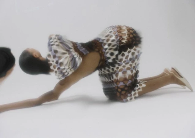 Model Raven Wallace in patterned textured dress kneeling on white seamless studio backdrop captured with motion blur.