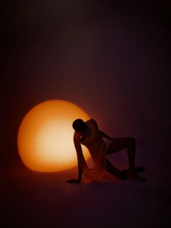 Model Raven Wallace posed before a large circular warm light source in a dark studio setting