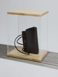 Dark brown leather handbag displayed inside a clear acrylic and wood vitrine resting on a slatted metal surface.