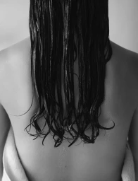 Monochrome rear view of a woman with long wet dark hair hanging down over her bare back.