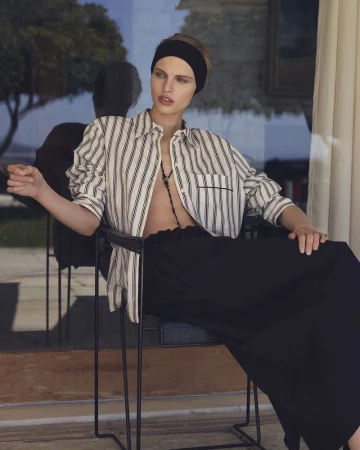 Model Karolina Spakowski seated outdoors wearing an unbuttoned striped shirt, black headband, and black skirt.