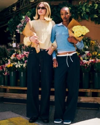Gigi Hadid and Divine Mugisha holding flower bouquets in knitwear outside a floral shop for Guest In Residence.