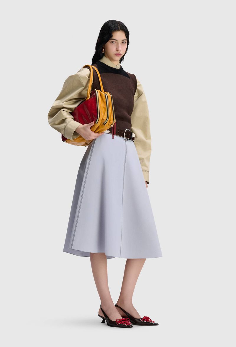 Model wearing a brown knit vest, beige puff-sleeve shirt, and powder blue A-line skirt against a grey studio backdrop.