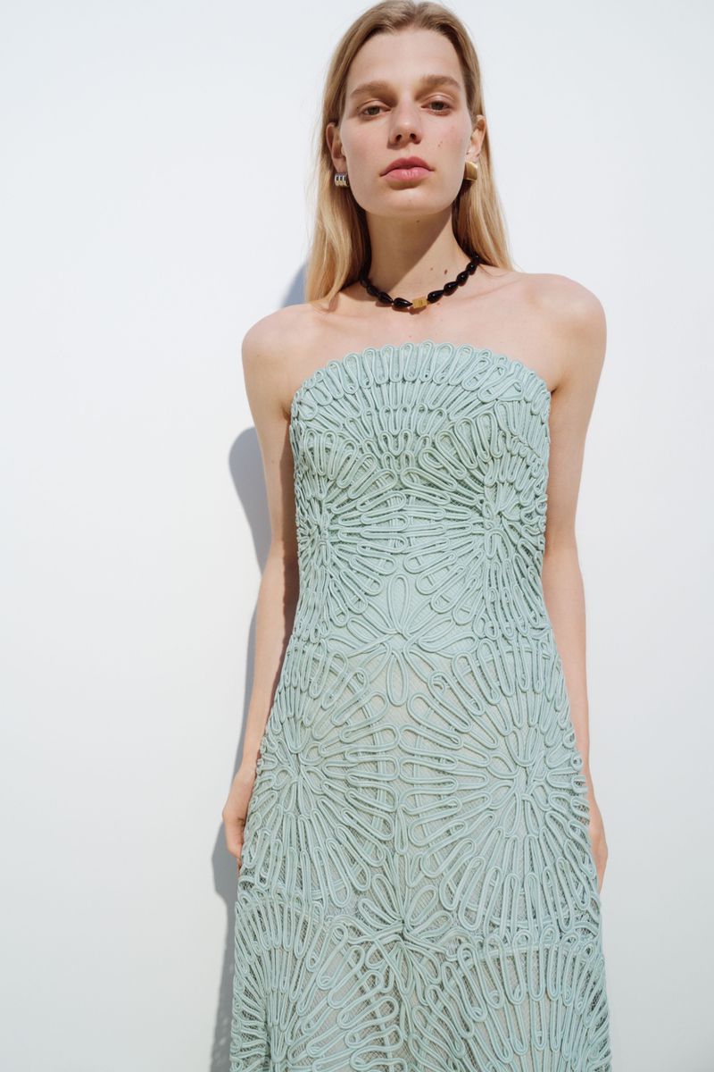 Model Saar Mansvelt Beck poses in a strapless mint green embroidered lace dress against a white studio background for Simkhai.