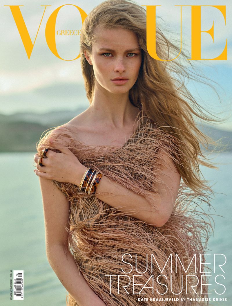 Model Kate Kraaijeveld wearing a textured feather dress with bracelets against an outdoor water background for Vogue Greece.