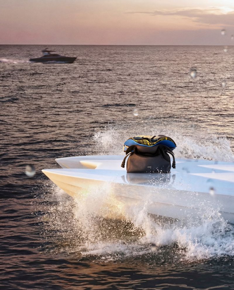 Loewe leather handbag placed on the white hull of a speedboat cruising through open ocean water at sunset.