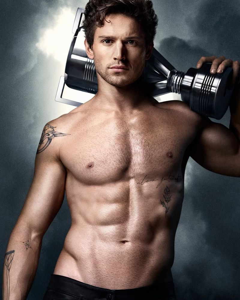 Model Giacomo Cavalli shirtless carrying a metallic trophy-shaped fragrance bottle on his shoulder against a stormy sky.