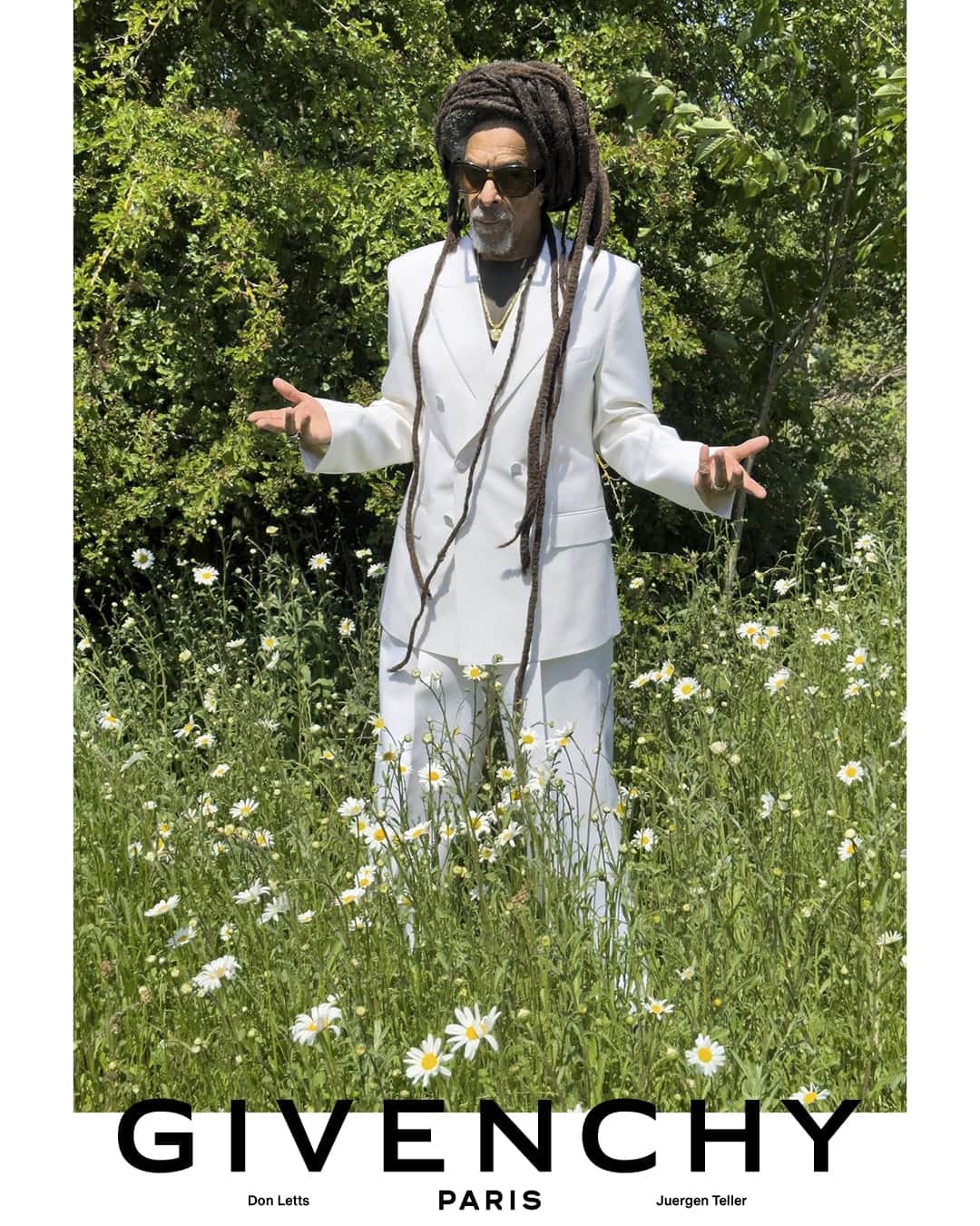 Don Letts standing in a meadow of white daisies wearing a white double-breasted suit and sunglasses for Givenchy.