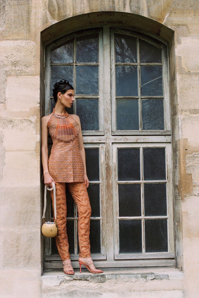 Fashionable woman in coordinated copper top and leggings strikes a pose leaning against an old window. Stylish couture fashion.