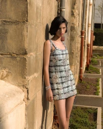Model in patterned tweed dress leaning against an aged stone wall outdoors for L'Officiel Belgium editorial