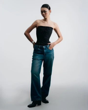 Portrait of a young Asian woman in a black tube top and denim jeans against a white backdrop in a fashion photography style.