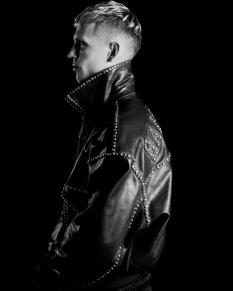 Black and white profile portrait of Dani Olmo wearing a black studded leather jacket against a black seamless backdrop.