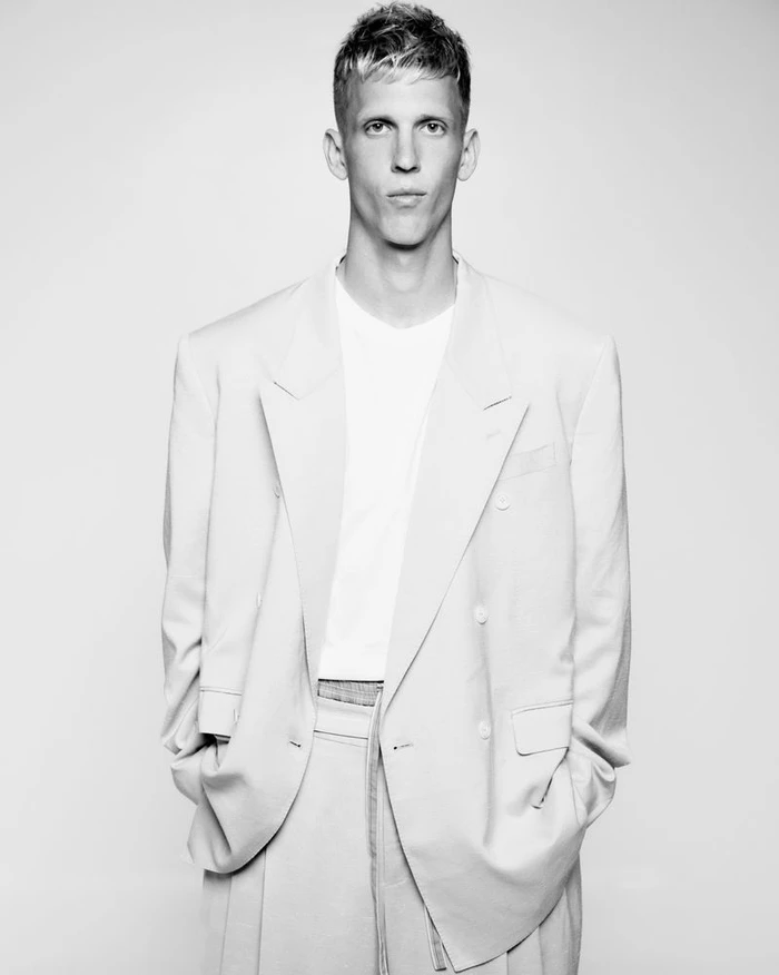 Dani Olmo wearing an oversized double-breasted light suit jacket and white t-shirt against a plain studio background.