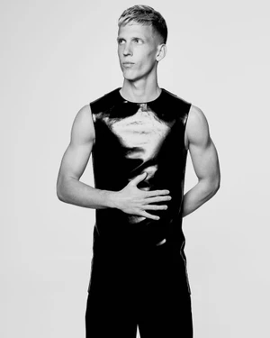 Black and white portrait of Dani Olmo posing in a sleeveless glossy black top against a white seamless background.