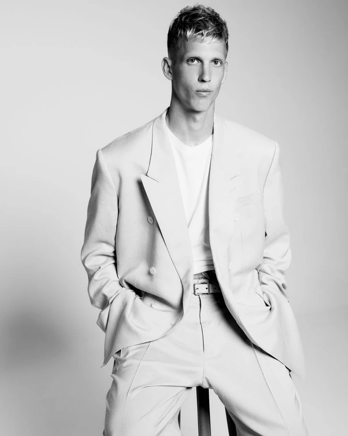 Dani Olmo seated in an oversized double-breasted suit and white t-shirt against a plain studio backdrop.