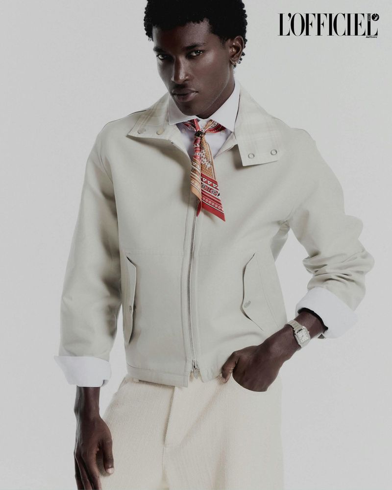 Model Gabriel Pitta wearing a cream zip-up jacket, patterned neck scarf, and wrist watch against a white studio background.