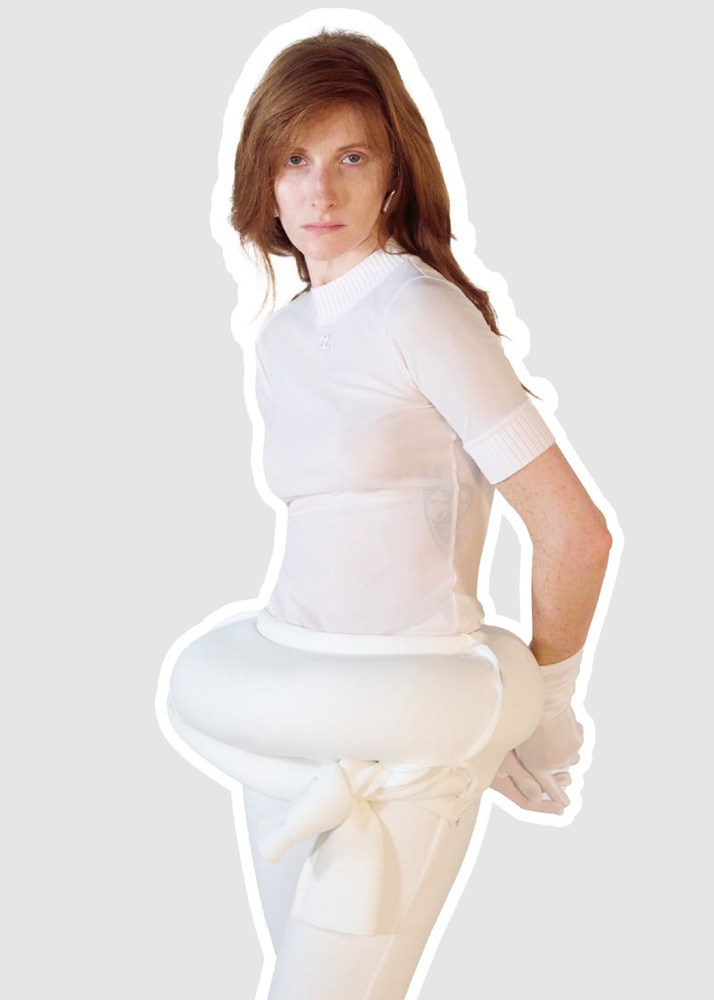 Model wearing a white short-sleeve top and white trousers with a rounded padded waist wrap against a plain background