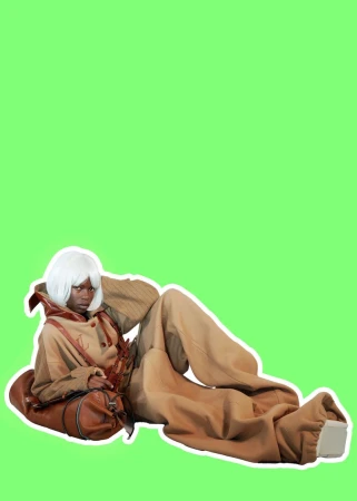 Model Adhieu Arok with a white bob wig reclining in an oversized camel suit against a solid green background.
