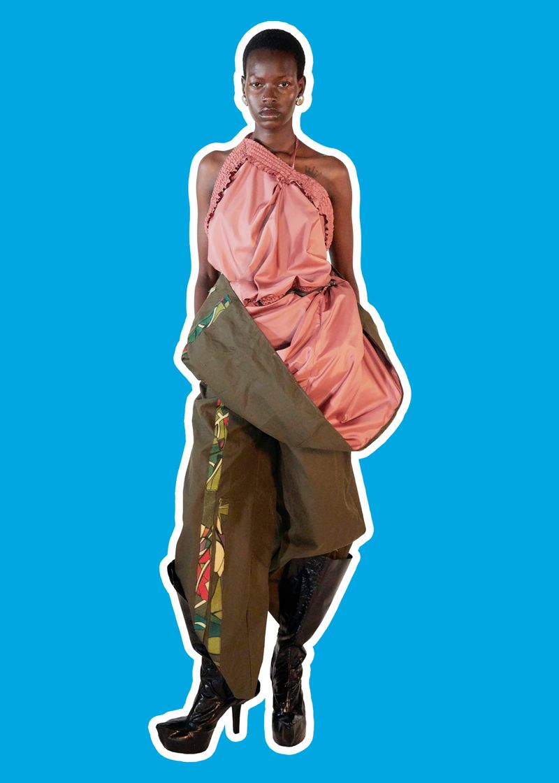 Model Adhieu Arok posing in a pink draped halter top and olive green wrap trousers against a vibrant blue background with white outline.