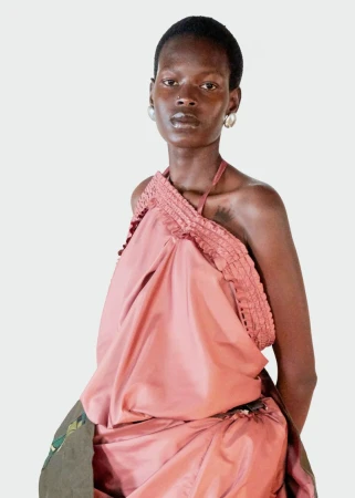 Model Adhieu Arok wearing a draped dusty rose halter top with ruffled trim against a plain white studio background.