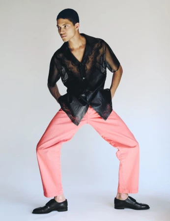Model wearing a sheer black short-sleeve shirt and pink trousers against a clean white background