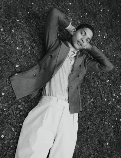 Model Jeranimo van Russel lying on grass with hands behind his head, wearing a tailored blazer and light trousers in black and white.