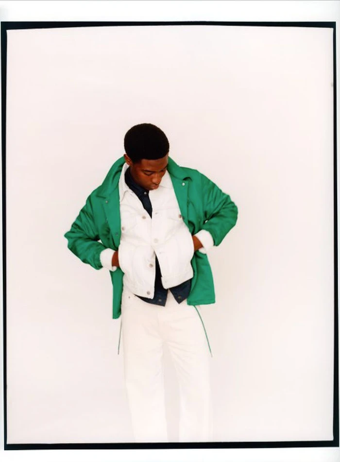 Model Momo Ciss wearing a bright green jacket layered over a white jacket and white pants against a seamless white background.