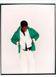 Model Momo Ciss wearing a bright green jacket layered over a white jacket and white pants against a seamless white background.