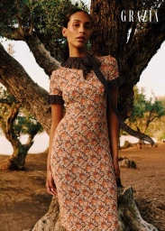 Model Anissa Bakhti poses in a floral dress with a polka dot scarf beside a large olive tree.