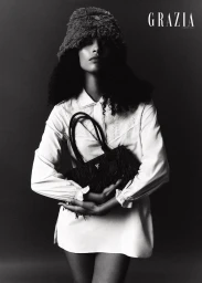 Model wearing a fuzzy bucket hat and white collared shirt holding a fringed handbag for a Grazia Middle East editorial