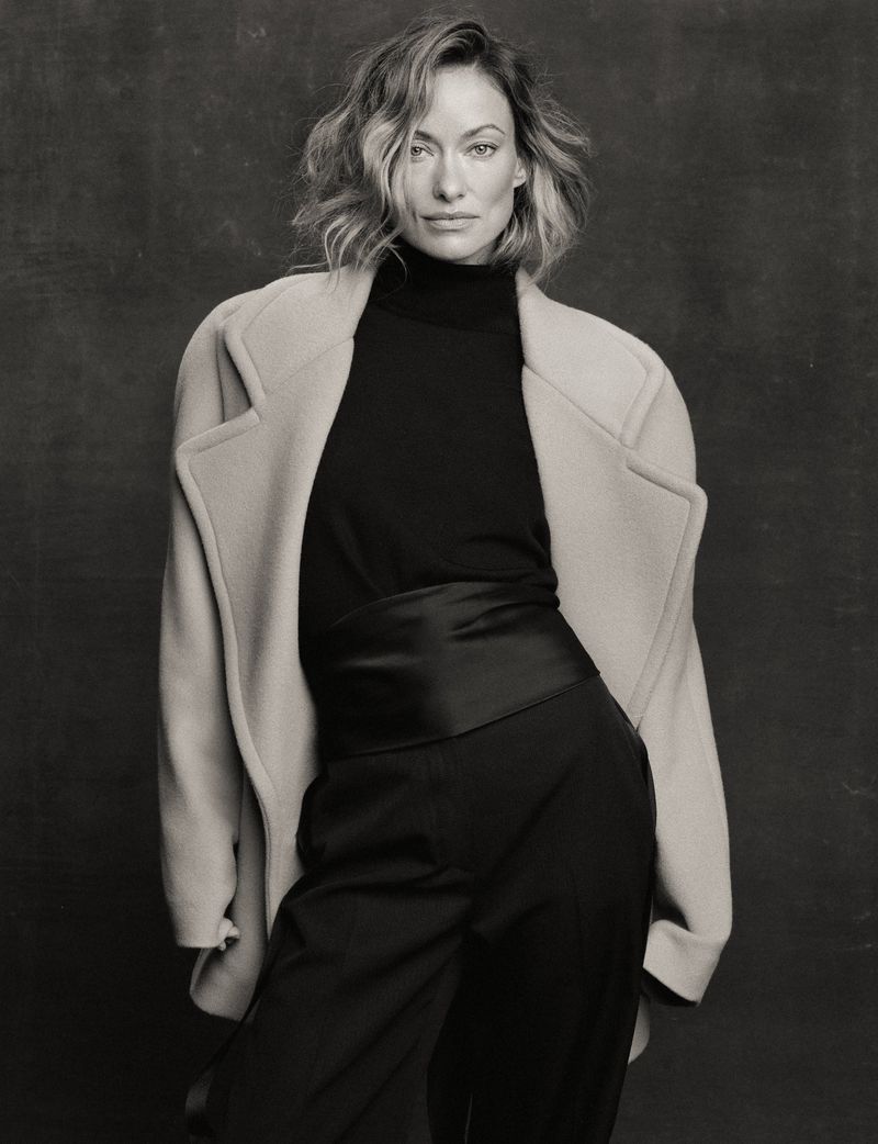 Olivia Wilde wearing a black turtleneck and light coat against a dark textured backdrop for The Cut editorial portrait
