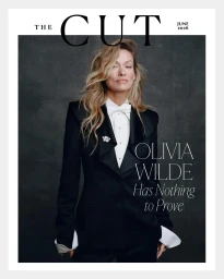 Olivia Wilde wearing a tailored black tuxedo with a white bow tie on the cover of The Cut against a dark textured backdrop.