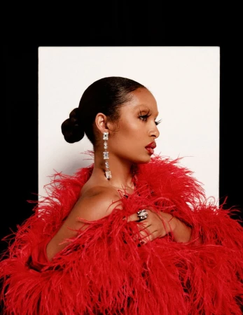 Yara Shahidi in a vibrant red feathered coat wearing crystal drop earrings against a white and black backdrop