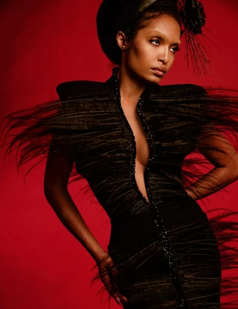 Yara Shahidi in a black feathered dress and dark headpiece against a deep red background for Numero Netherlands.