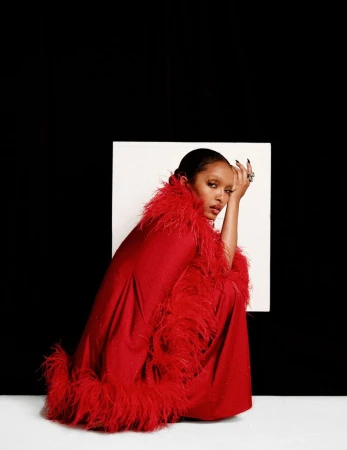 Yara Shahidi crouching against a white and black background wearing a red feather-trimmed coat for Numero Netherlands.