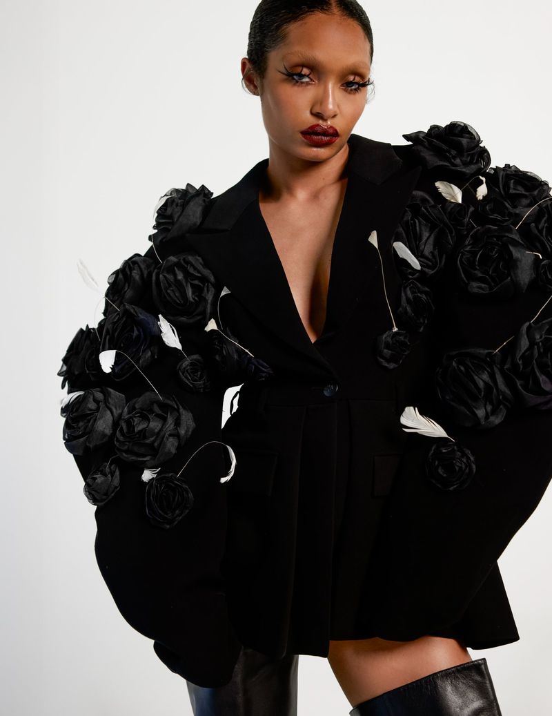 Yara Shahidi poses in an oversized black blazer adorned with 3D fabric roses against a white studio background.