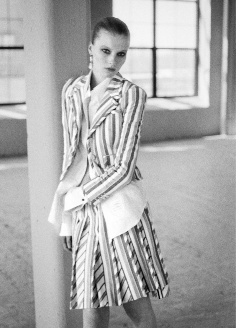 Model Lainey Hearn in a striped blazer and skirt leaning against a column in an interior space for The Greatest Magazine.