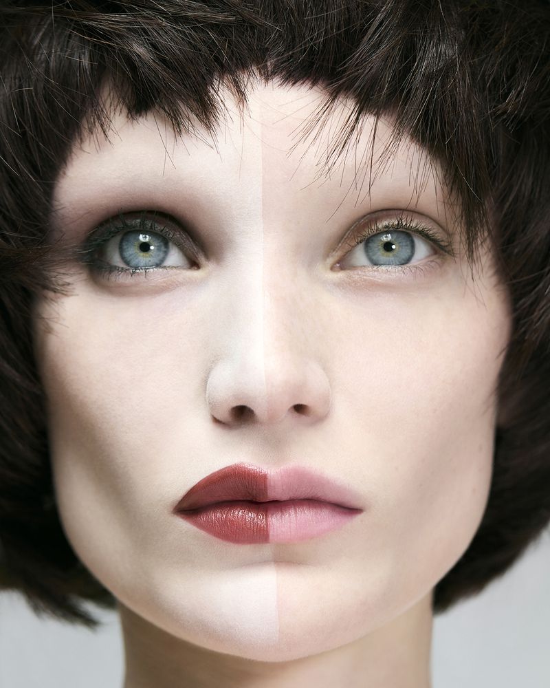 Close-up portrait of a woman with contrasting split makeup and dark layered hair for Twin Magazine