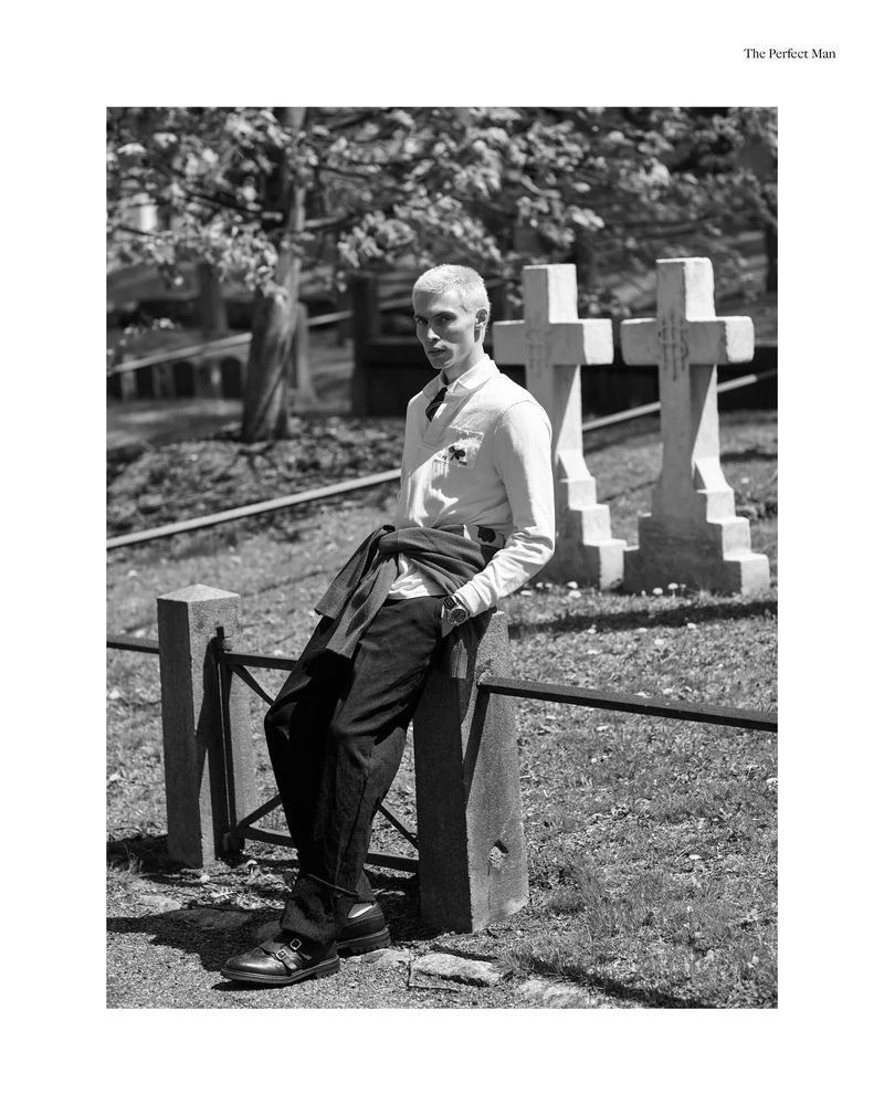 Monochrome fashion editorial portrait of a male model leaning against a fence in a cemetery with headstones