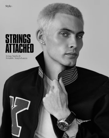 Model Arnau Sarda posing in a black zip jacket with striped collar and wristwatch against a neutral studio backdrop.