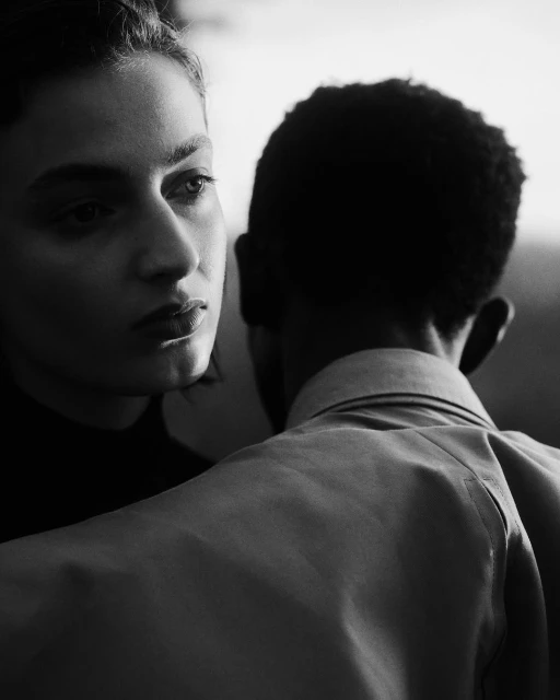 Black and white portrait of a Caucasian woman and a Black man wearing a collared shirt, captured with soft, diffused lighting.