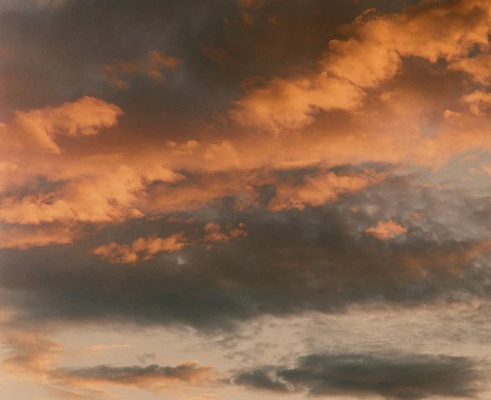 Dramatic sunset sky filled with dense, layered clouds lit in warm golden and orange hues against dark grey undertones.