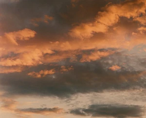 Dramatic sunset sky filled with dense, layered clouds lit in warm golden and orange hues against dark grey undertones.
