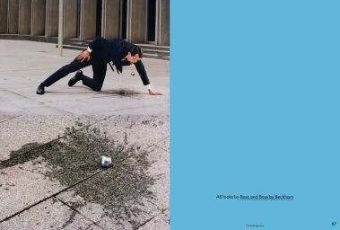 Editorial double-page spread with a man in a dark suit crawling on stone pavement next to a small metallic orb.