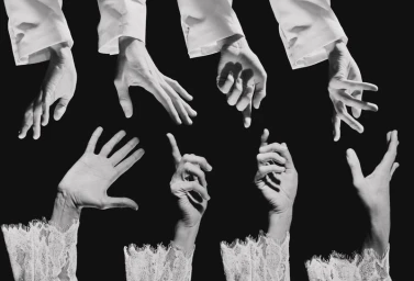 Gesturing hands in white lace and tailored shirt cuffs reaching toward each other against a solid black background.