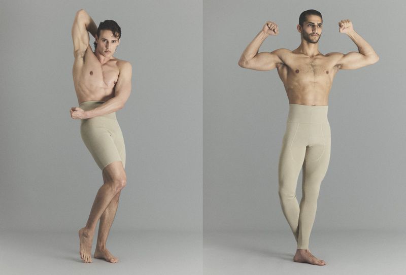 Two shirtless male models posing in beige high-waisted tights against a neutral grey studio background.