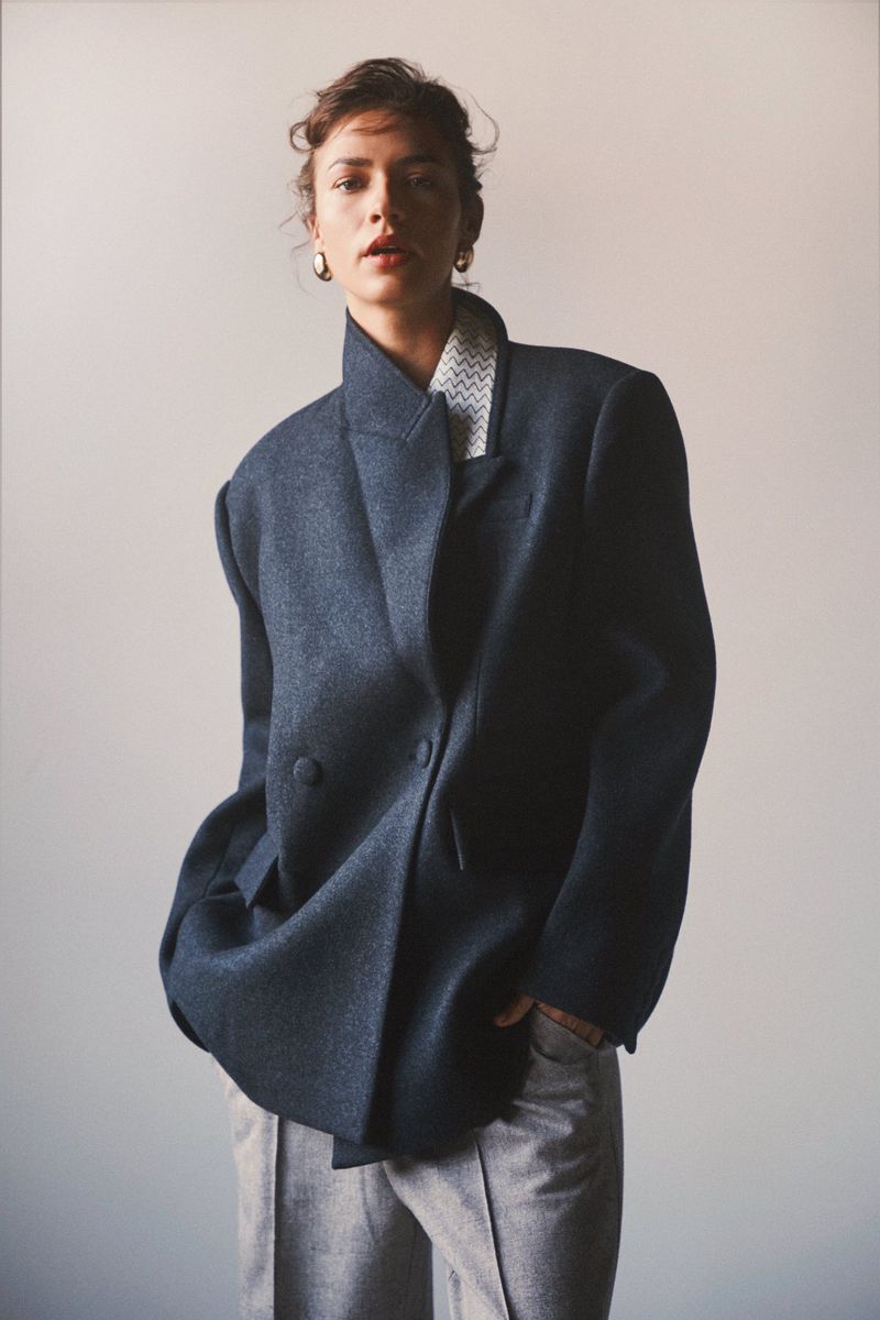 Fashion model posing in an oversized navy wool blazer and grey tailored trousers against a neutral studio backdrop.