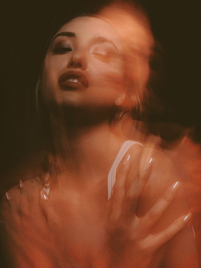 Bella Podaras posing with hands near her chest in a motion-blurred, warm-toned editorial portrait.